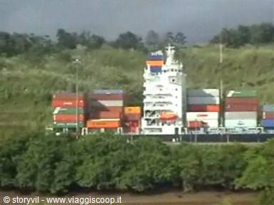 Container ship loaded with colored boxes, backed by green hills