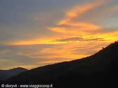 Orange clouds glowing across the sky above the dark hillside