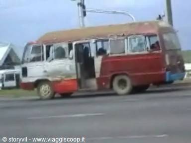 Rusty red and white bus speeding along an asphalted city road