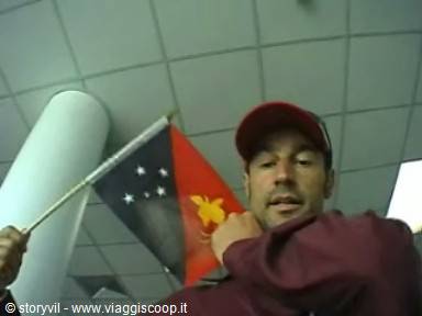 Traveler in red cap holds Papua New Guinea flag indoors, column behind