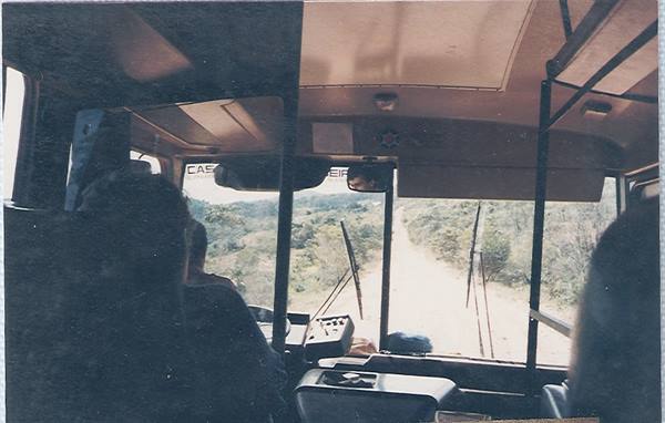 Bus interior with passengers along a dirt road through wooded hills