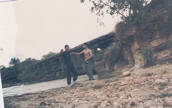 Two guys on the rocky riverbank under an old wooden bridge