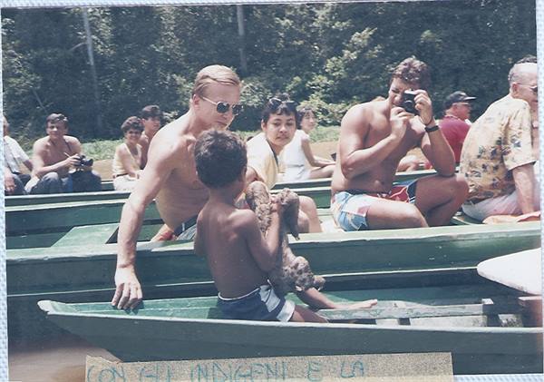 Tourists in a green wooden canoe with an indigenous child among the forest