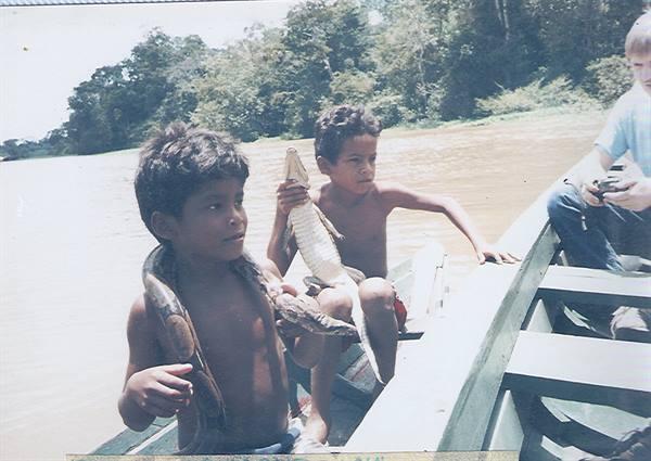 Children on wooden boat holding a snake and small caiman
