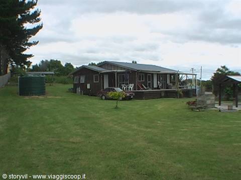 Wooden countryside house, green lawn, water tank, cloudy sky
