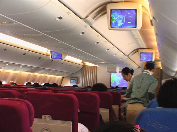Flight attendant assists passengers in cabin with red seats and screens
