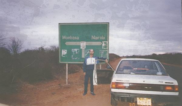 Man next to a white car beneath the Mombasa-Nairobi road sign