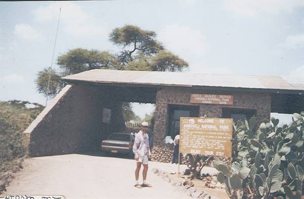 Tourist in light shirt standing at the Arusha National Park entrance gate