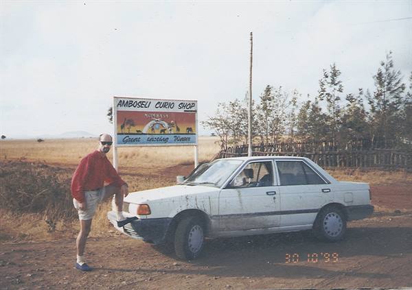 Tourist leaning on a white Nissan in front of the Amboseli Curio Shop sign