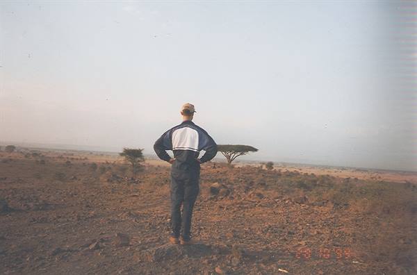 Man in cap and blue jacket among acacia trees on dry African ground