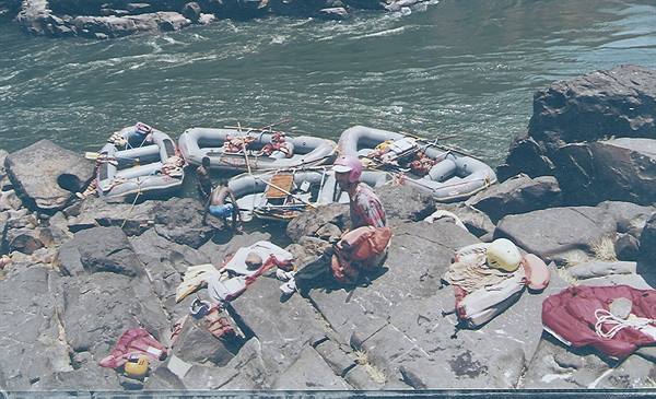 Inflatable rafts on grey rocks beside the river, gear scattered around