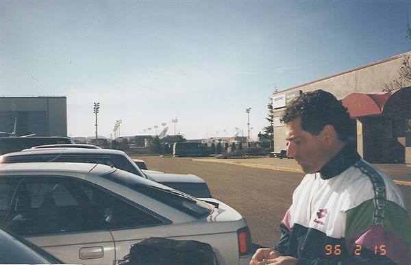 Man in sports jacket beside parked cars, airport runways in the background