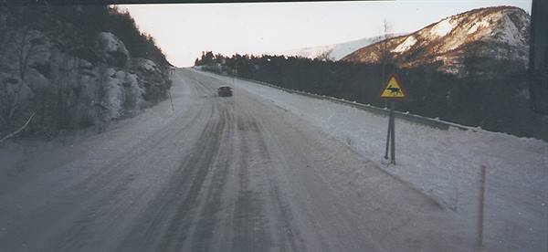 Car driving on snowy road, slippery road sign, snow-covered rocky mountains