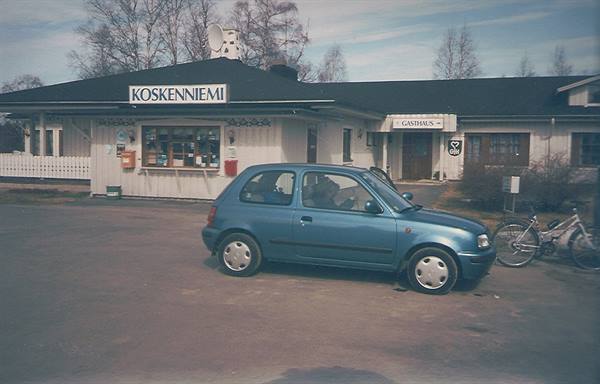 Blue car parked in front of Koskenniemi store, bicycle nearby, grey daylight
