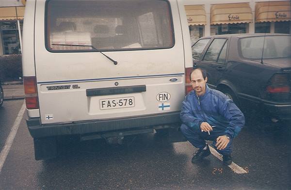 Man squatting with a cigarette next to a Ford Transit van with Finnish plates