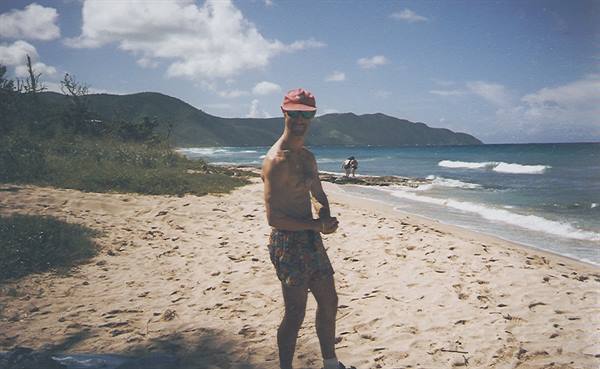 Boy in red cap and shorts on sandy beach, waves and green hills