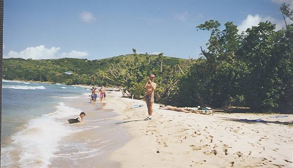 Tourists on a tropical sandy beach, man sunbathing, swimmers in the waves