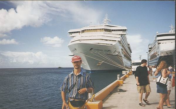 Tourist in red cap beside large Carnival cruise ship docked at pier