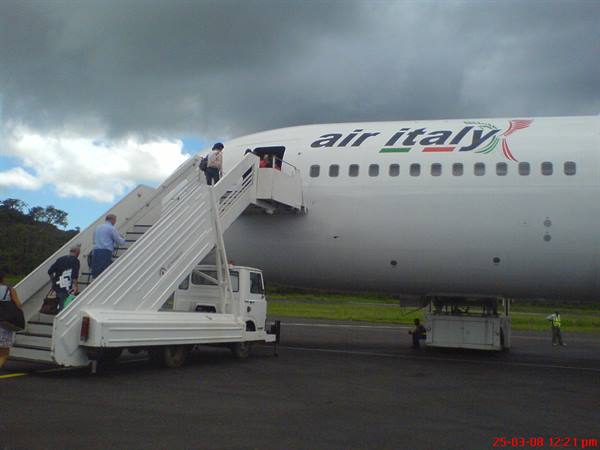 Passengers board an Air Italy Boeing via mobile stairs under cloudy skies