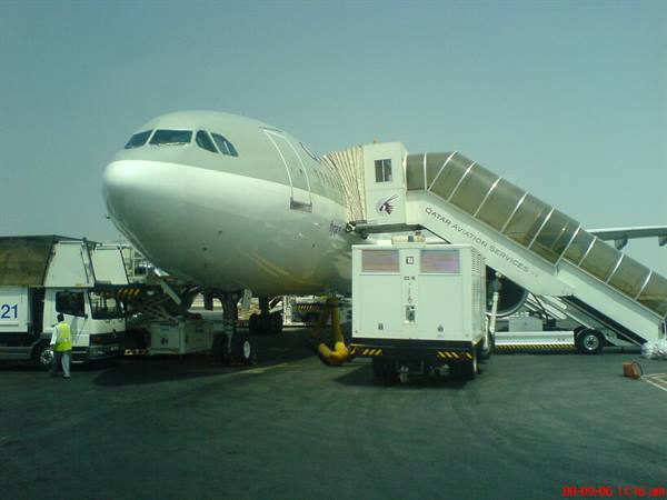 Qatar Airways aircraft parked with mobile boarding stairs and ground vehicles on tarmac
