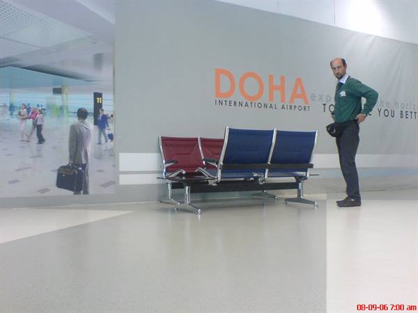 Man standing next to red and blue seats at Doha International Airport