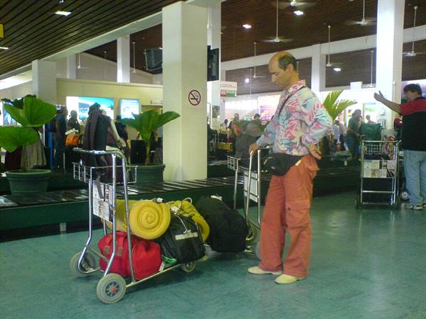 Man in floral shirt with luggage cart inside airport baggage hall