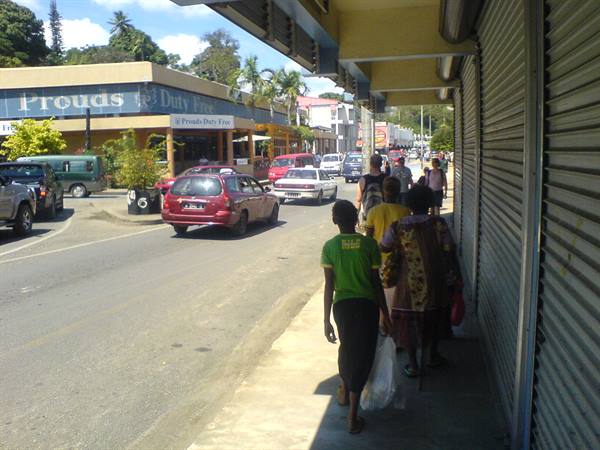 Pedestrians walking past a shuttered storefront, cars passing Prouds Duty Free shop