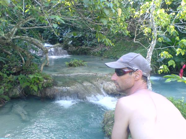 Man in cap and sunglasses by limestone cascades surrounded by lush tropical vegetation