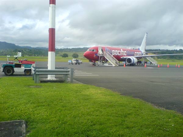 Red Pacific jet with boarding stairs on tarmac, grey sky, green grass
