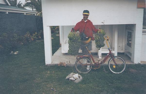 Man in cap holding two bunches of bananas next to a red bicycle