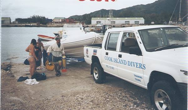 White Cook Island Divers pickup truck loading dive tanks beside inflatable boat on shore