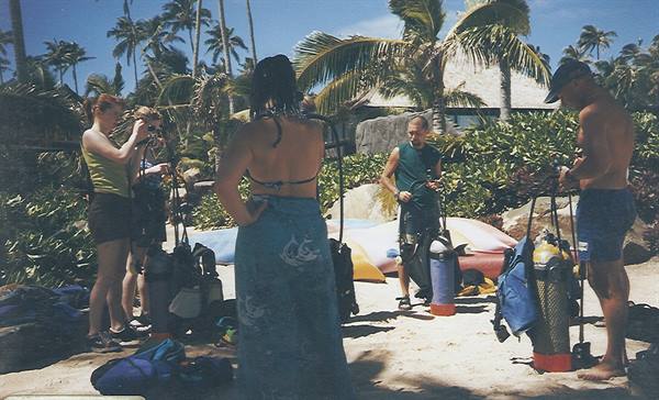 Divers prepare scuba tanks and gear on a palm-fringed beach