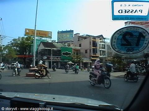 Busy motorbike intersection in a Vietnamese city, woman in pink costume riding scooter