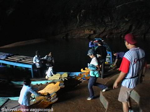 Tourists stepping down to wooden boats inside dark cave, dim lights