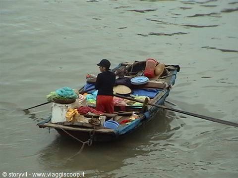 Woman rows a wooden boat loaded with baskets and colorful fabrics