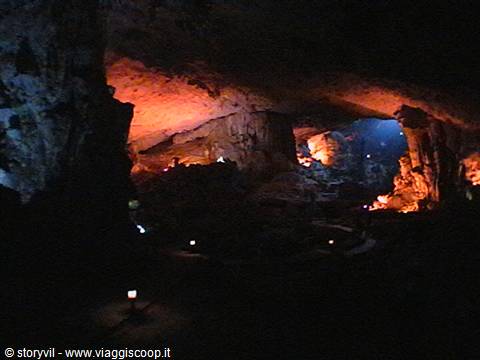 Cave lit by orange lights among limestone stalactites and stalagmites