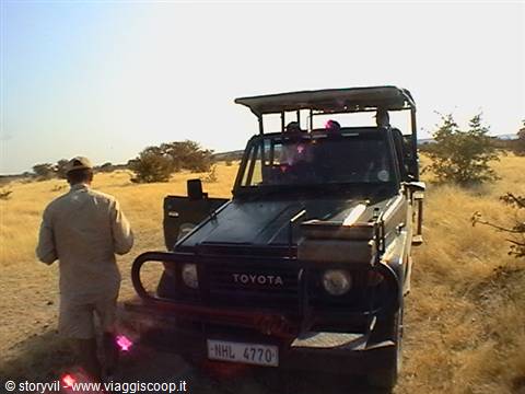 Guide standing next to a Toyota safari truck in dry savanna grass