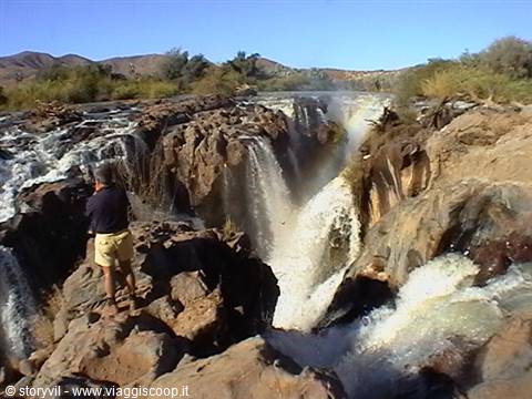Man on volcanic rocks watching Epupa Falls cascading through white foam