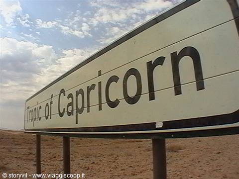 Metal Tropic of Capricorn road sign standing in sandy desert under cloudy sky