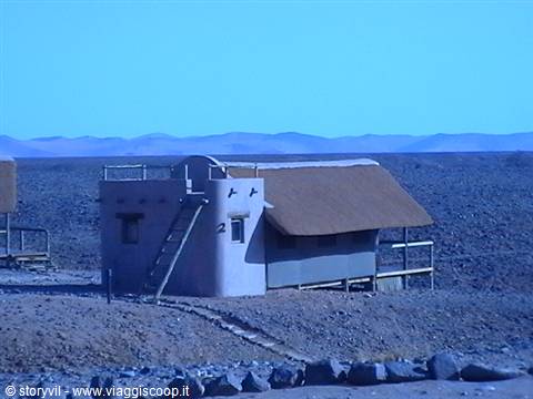 Mud and thatch bungalow on a rocky desert plain with blue mountains
