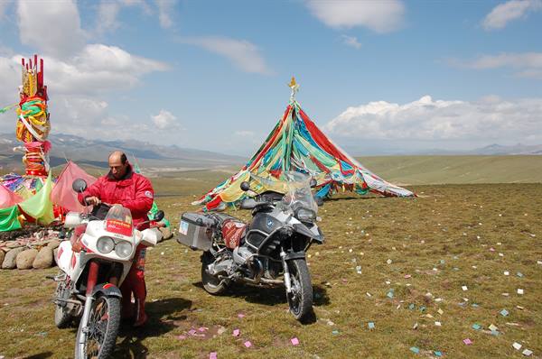 Motorcyclists on grassland beside a Tibetan oboo with colorful prayer flags