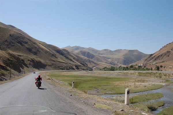 Motorcyclist in red helmet on asphalt road between dry hills and green valley
