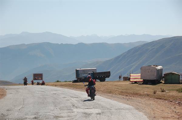 Motorcyclist on mountain road, trucks and wagons parked among the hills