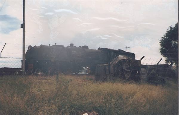 Abandoned steam locomotive behind a wire fence, dry grass, cloudy sky