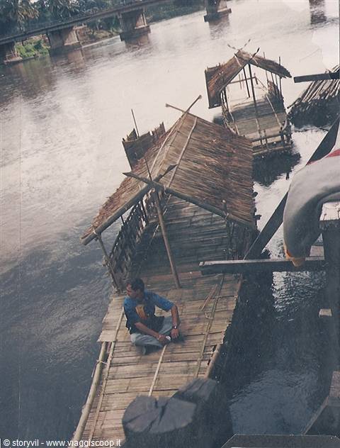 Man sitting on bamboo raft with thatched hut on the river