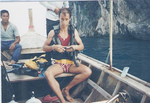 Diver prepares scuba gear on wooden boat near limestone cliffs