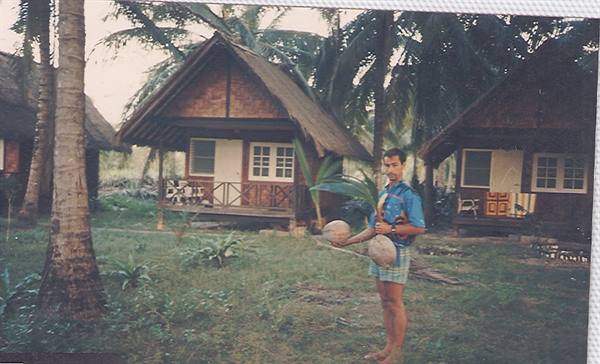 Man holding coconuts between thatched bungalows and palm trees