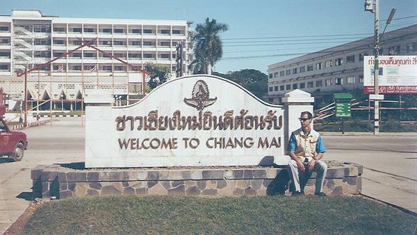 Tourist sitting on stone wall beside the white welcome sign of Chiang Mai