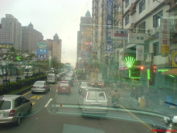 City traffic seen through bus window, cars and neon signs between buildings