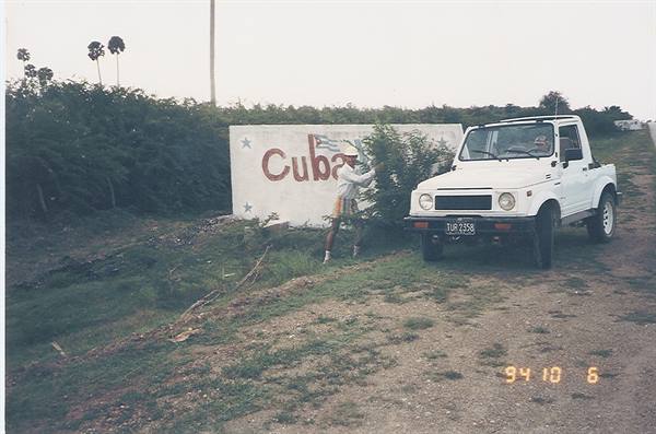 Tourist beside a sign reading Cuba and a white off-road vehicle